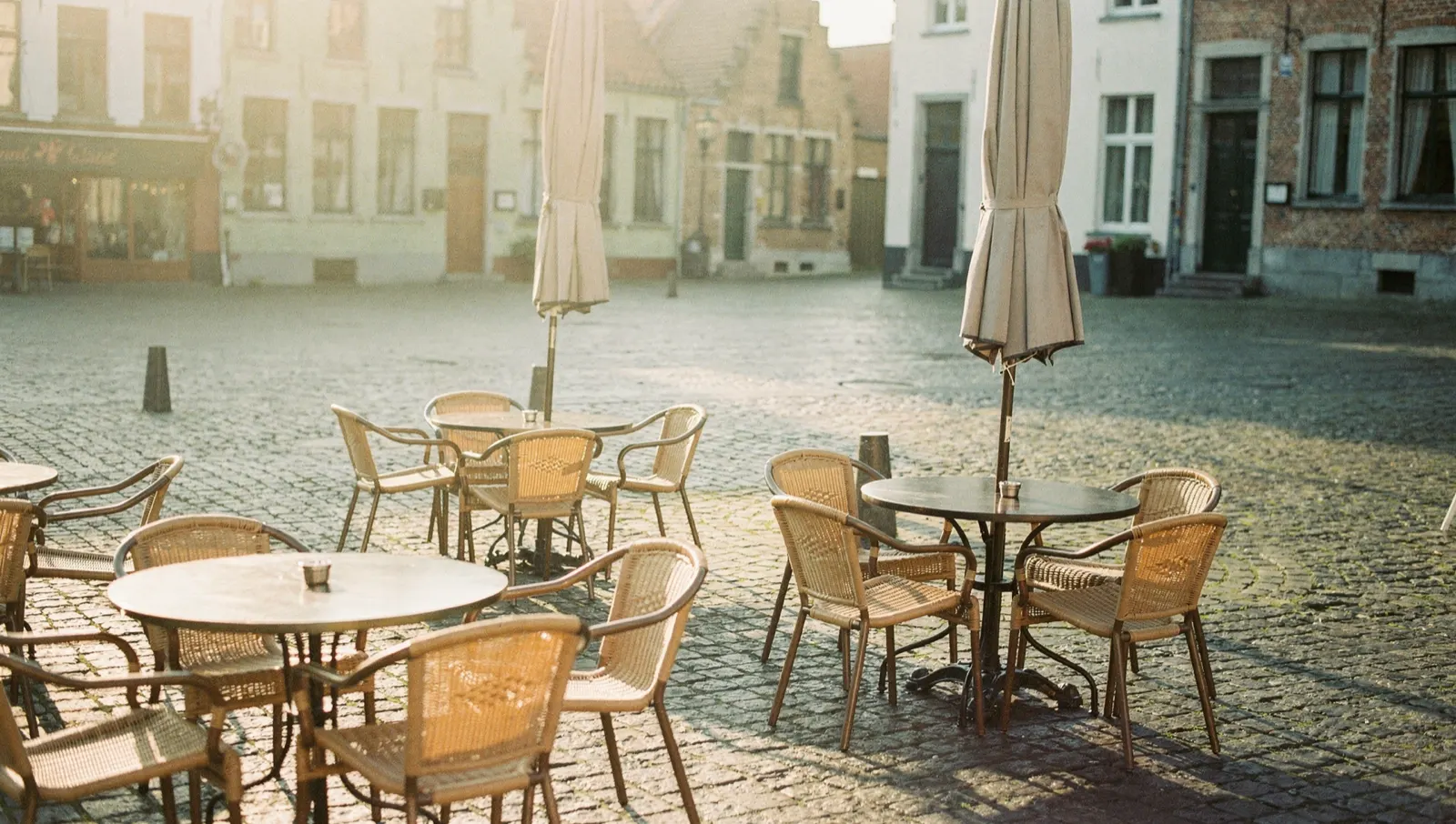 A café terrace on cobbles at first light, the parasols still closed