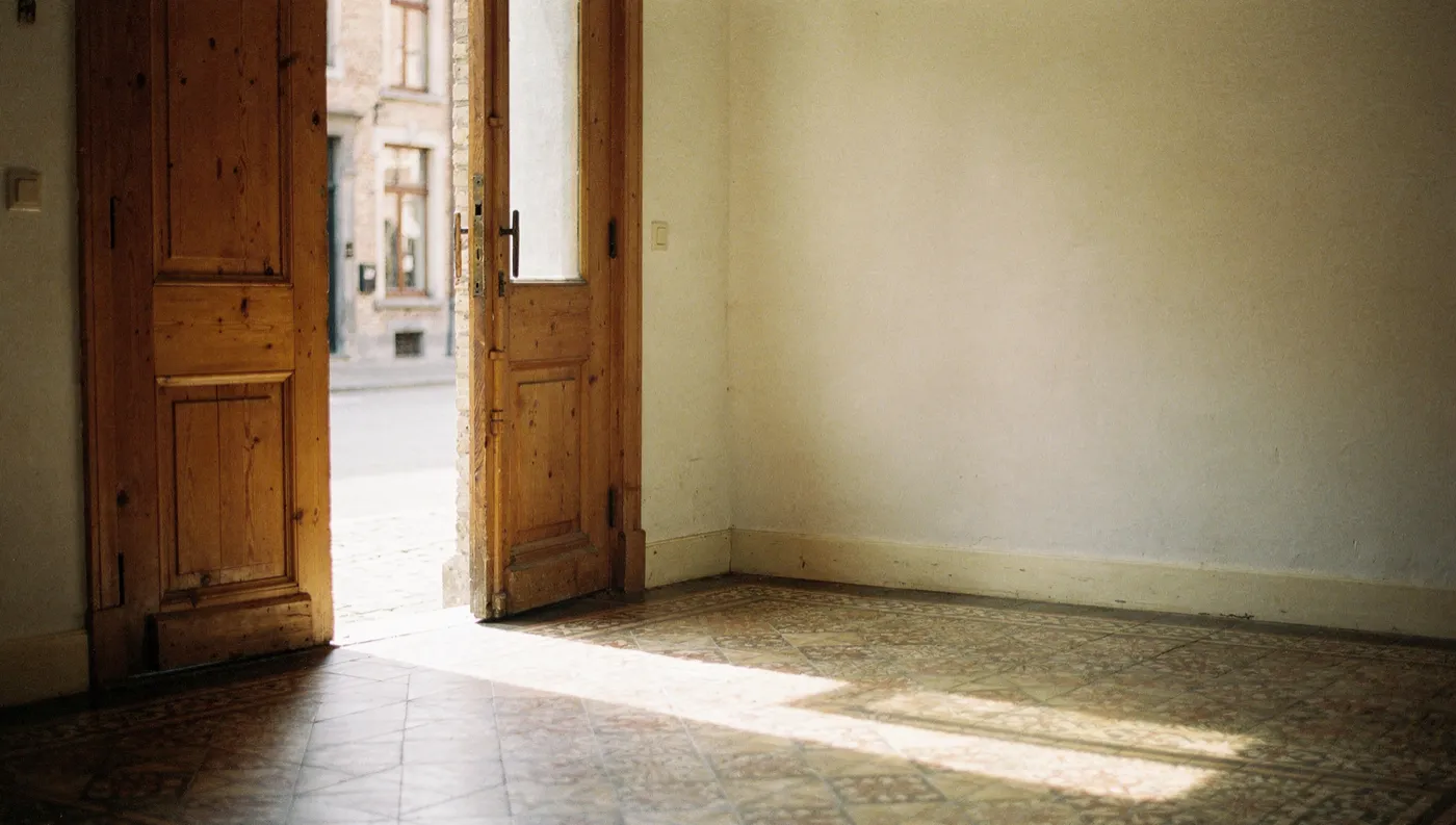The hall of a Flemish townhouse with the front door standing open onto a sunlit street