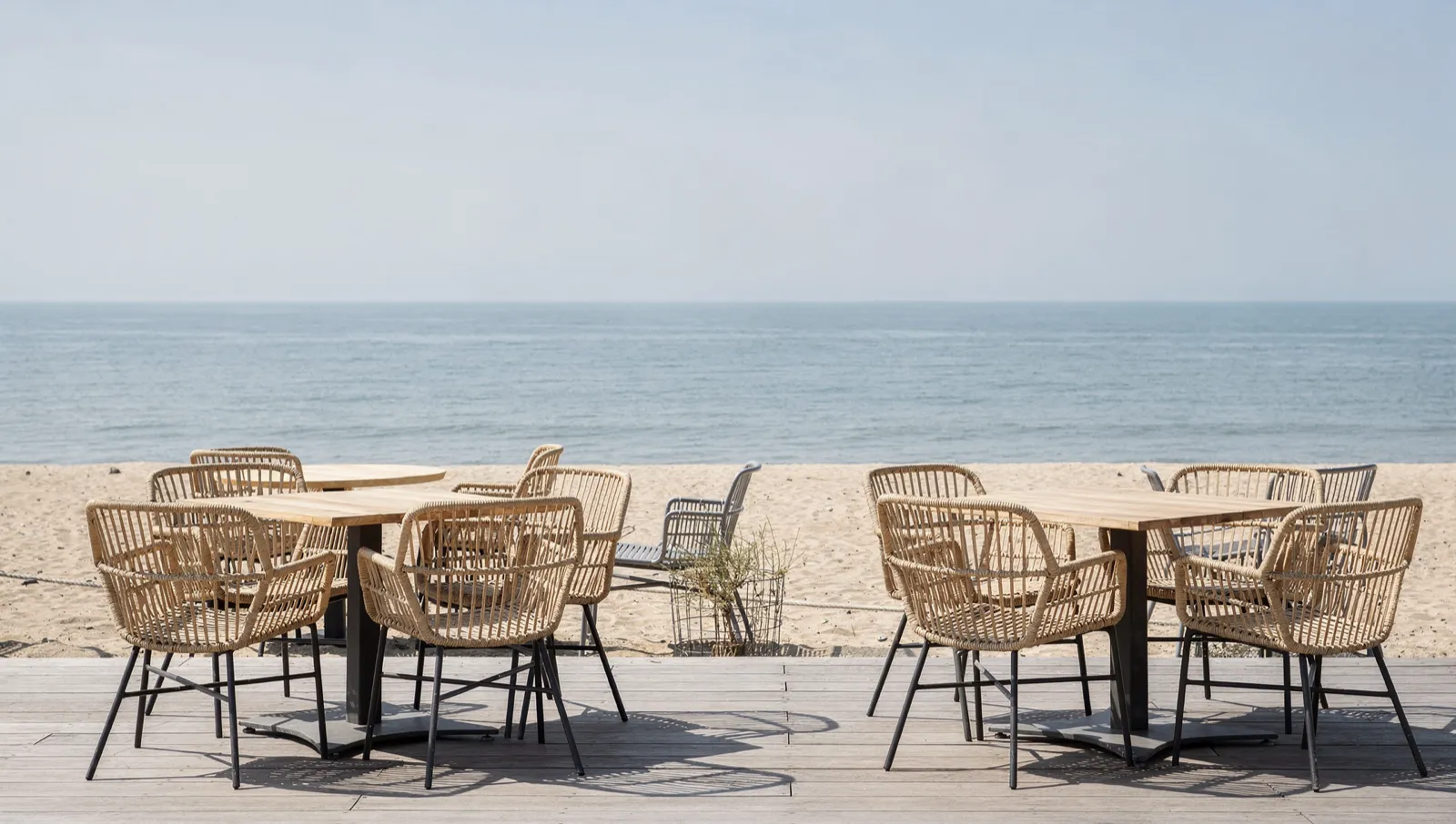 Rattan chairs and timber tables on decking facing an empty beach and the sea