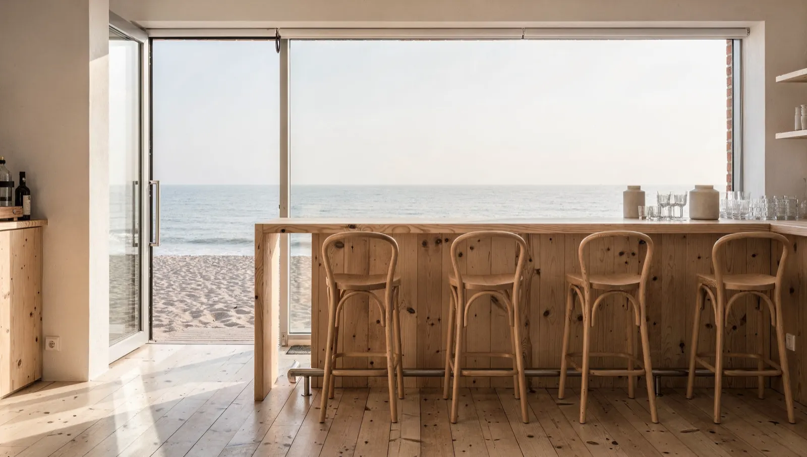 A beach bar counter with bentwood stools and the sea through an open frontage
