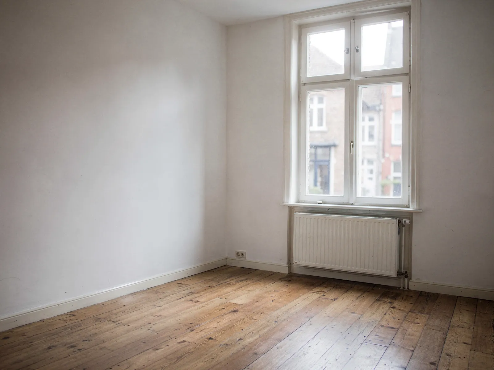 An empty living room in a Flemish townhouse with a wooden floor and tall windows onto the street